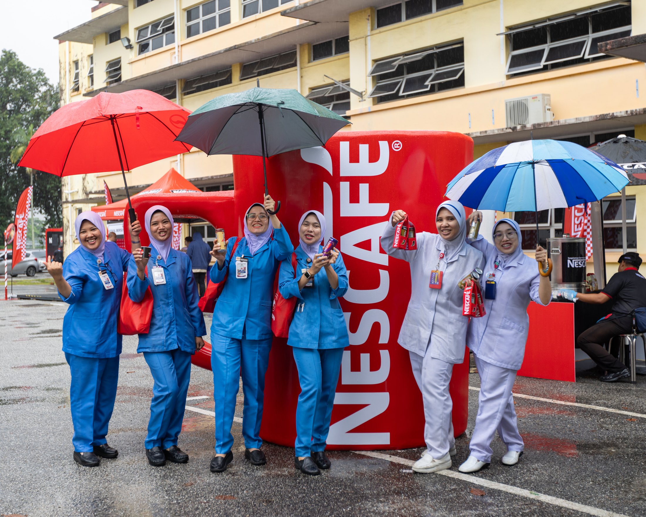 Healthcare frontliners standing in the rain with NESCAFÉ drinks during the Johor Bahru hospital initiative